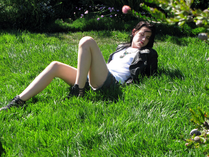 Kristen Stewart lyins back in the grass in cutoff shorts, white tshirt & black lether jacket