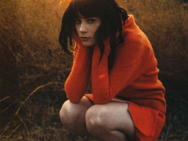Zooey Deschanel crouches in orange sweater and skirt